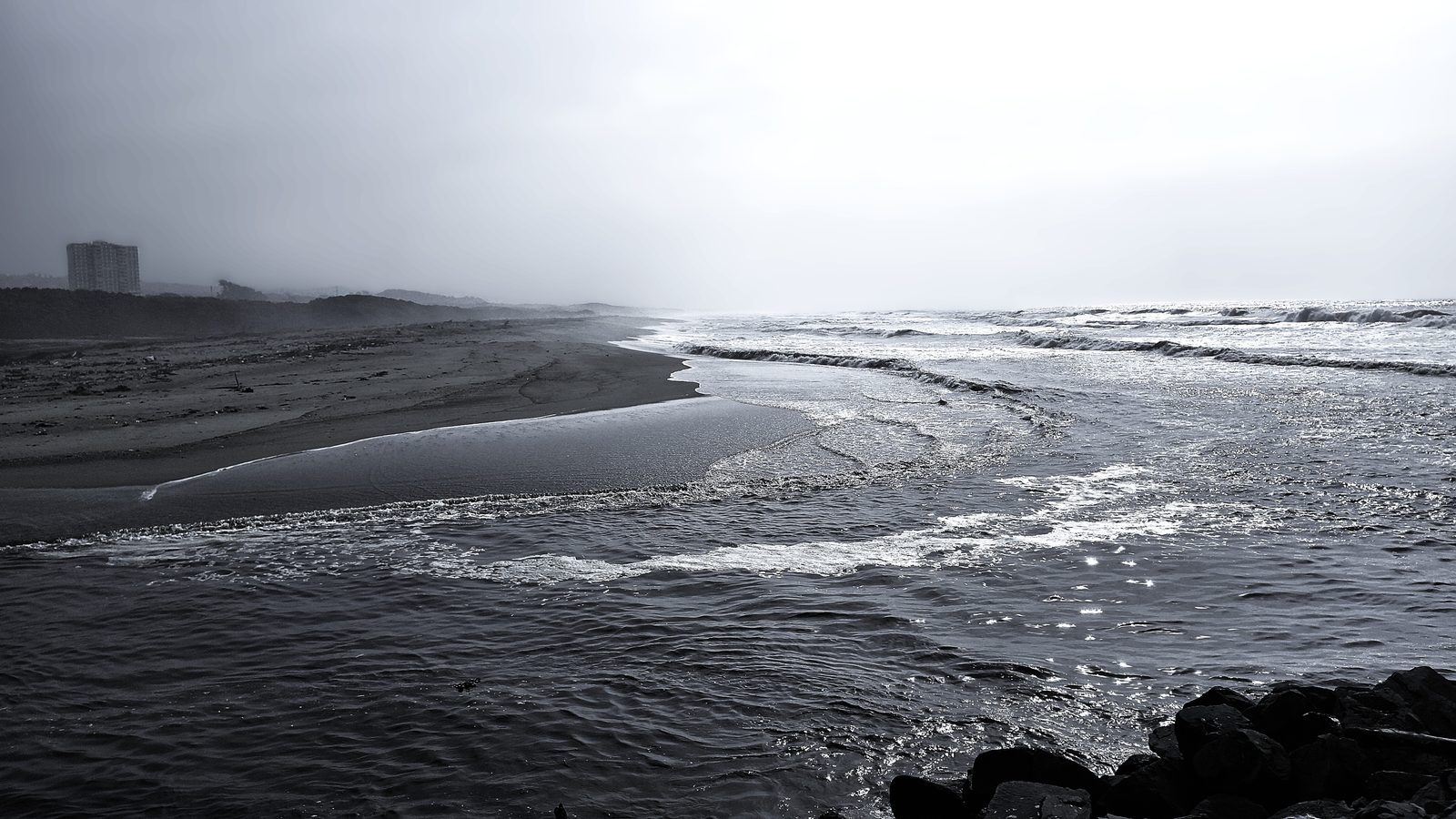Misty high-contrast beach with distant tower in fog